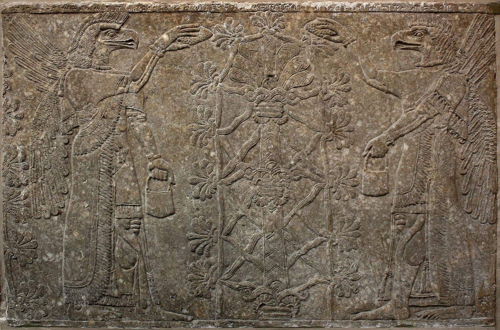 A carved stone relief showing winged, eagle-headed figures beside a stylised tree.