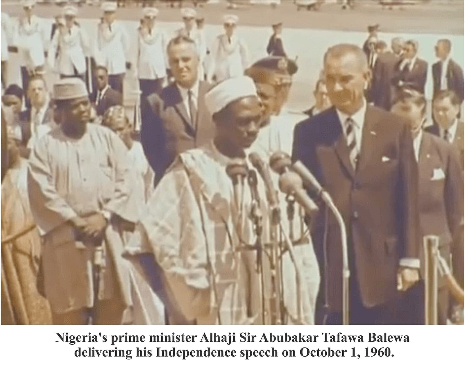 A man in robes speaking at a microphone before an assembly.