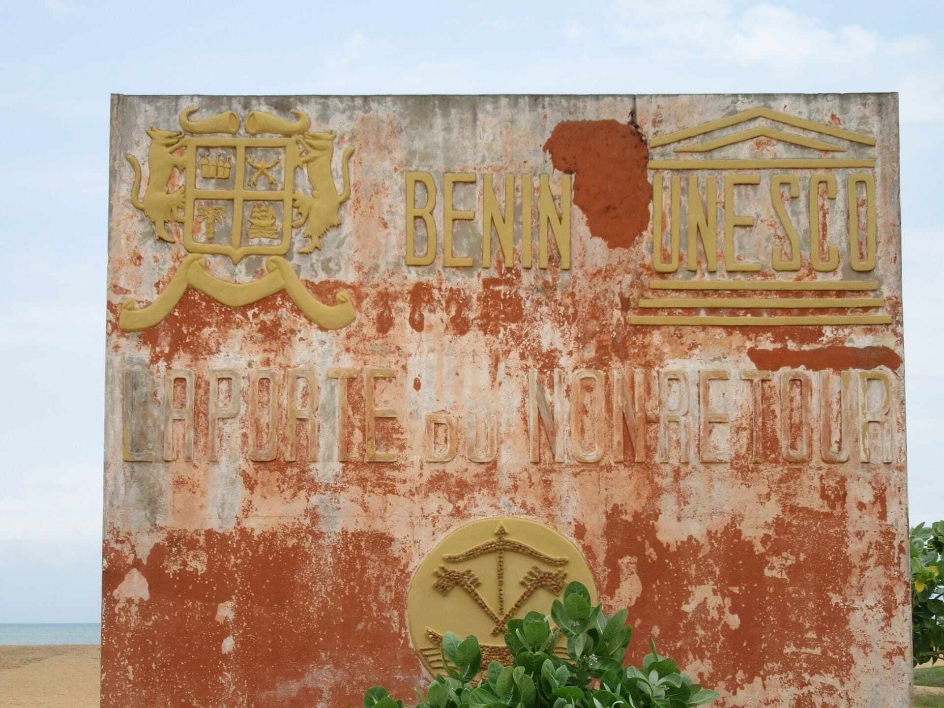 A weathered Benin and UNESCO sign at the Door of No Return in Ouidah.